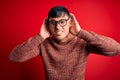 Young handsome hispanic man wearing nerd glasses over red background Trying to hear both hands on ear gesture, curious for gossip