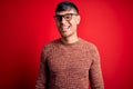 Young handsome hispanic man wearing nerd glasses over red background winking looking at the camera with sexy expression, cheerful Royalty Free Stock Photo