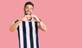 Young handsome hispanic man wearing striped tshirt smiling in love doing heart symbol shape with hands