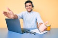 Young handsome hispanic man working at the office wearing operator headset looking at the camera smiling with open arms for hug Royalty Free Stock Photo