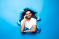 Young handsome indian bearded man talk phone look from blue paper hole Royalty Free Stock Photo