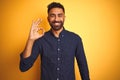 Young handsome indian businessman wearing shirt over isolated yellow background smiling positive doing ok sign with hand and Royalty Free Stock Photo