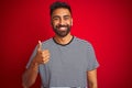 Young handsome indian man wearing navy striped t-shirt over isolated red background doing happy thumbs up gesture with hand Royalty Free Stock Photo