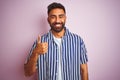 Young handsome indian man wearing summer striped shirt over isolated pink background doing happy thumbs up gesture with hand Royalty Free Stock Photo