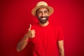 Young handsome indian man wearing t-shirt and hat over isolated red background doing happy thumbs up gesture with hand Royalty Free Stock Photo