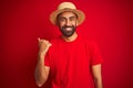 Young handsome indian man wearing t-shirt and hat over isolated red background smiling with happy face looking and pointing to the Royalty Free Stock Photo