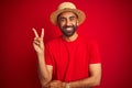 Young handsome indian man wearing t-shirt and hat over isolated red background smiling with happy face winking at the camera doing Royalty Free Stock Photo