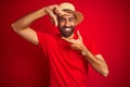 Young handsome indian man wearing t-shirt and hat over isolated red background smiling making frame with hands and fingers with Royalty Free Stock Photo