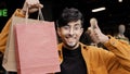 Young handsome joyful guy stands in boutique holding paper bags points for good buy happy stylish man in clothing store Royalty Free Stock Photo