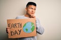 Young handsome latin man holding banner asking for earth and enviroment conservation serious face thinking about question, very Royalty Free Stock Photo