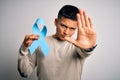 Young handsome latin man holding blue cancer ribbon over isolated white background with open hand doing stop sign with serious and Royalty Free Stock Photo