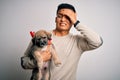 Young handsome latin man holding cute puppy pet over isolated white background stressed with hand on head, shocked with shame and Royalty Free Stock Photo