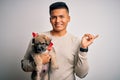 Young handsome latin man holding cute puppy pet over isolated white background very happy pointing with hand and finger to the Royalty Free Stock Photo