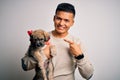 Young handsome latin man holding cute puppy pet over isolated white background very happy pointing with hand and finger Royalty Free Stock Photo