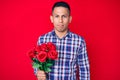 Young handsome latin man holding flowers thinking attitude and sober expression looking self confident