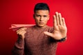 Young handsome latin man holding paper plane over isolated red background with open hand doing stop sign with serious and Royalty Free Stock Photo