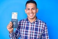 Young handsome latin man holding united states passport and boarding pass looking positive and happy standing and smiling with a Royalty Free Stock Photo