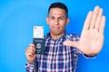 Young handsome latin man holding united states passport and boarding pass with open hand doing stop sign with serious and Royalty Free Stock Photo