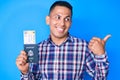 Young handsome latin man holding united states passport and boarding pass pointing thumb up to the side smiling happy with open Royalty Free Stock Photo