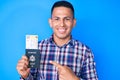 Young handsome latin man holding united states passport and boarding pass smiling happy pointing with hand and finger Royalty Free Stock Photo