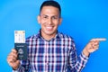 Young handsome latin man holding united states passport and boarding pass smiling happy pointing with hand and finger to the side Royalty Free Stock Photo