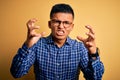 Young handsome latin man wearing casual shirt and glasses over yellow background Shouting frustrated with rage, hands trying to Royalty Free Stock Photo