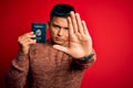 Young handsome latin tourist man on vacation holding united states passport id with open hand doing stop sign with serious and Royalty Free Stock Photo