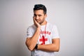 Young handsome lifeguard man with beard wearing t-shirt with red cross and whistle thinking looking tired and bored with