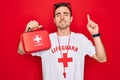 Young handsome lifeguard man wearing t-shirt with red cross and whistle holding first aid kit surprised with an idea or question