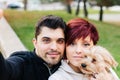 A young, handsome, light-eyed couple taking a selfie outdoors with their dog while walking in the city park Royalty Free Stock Photo