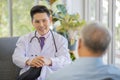 A young handsome male asian doctor wearing white lab coat with stethoscope sitting on sofa talking and advising to old fat gray Royalty Free Stock Photo