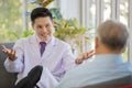 A young handsome male asian doctor wearing white lab coat with stethoscope sitting on sofa talking and advising to old fat gray Royalty Free Stock Photo