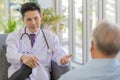 A young handsome male asian doctor wearing white lab coat with stethoscope sitting on sofa talking and advising to old fat gray Royalty Free Stock Photo