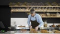 Young handsome man in the apron and gloves bringing fresh pies to the counter in the bakery shop. Indoors