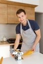 Young handsome man in apron rolling dough in modern kitchen. Chef making pasta with pasta cutter machine. Concept of homemade food Royalty Free Stock Photo