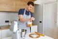 Young handsome man in apron sifting flour in modern kitchen. Concept of homemade bakery food, male cooking and domestic lifestyle Royalty Free Stock Photo