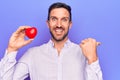 Young handsome man asking for health care holding red heart over isolated purple background pointing thumb up to the side smiling Royalty Free Stock Photo