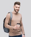 Young handsome man with backpack holding coffee cup isolated on gray background. Smiling student or businessman studio portrait Royalty Free Stock Photo