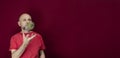 Young handsome man with beard, bald head and red shirt standing tossing pinecone fruit up against red background