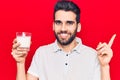 Young handsome man with beard drinking glass of milk smiling happy pointing with hand and finger to the side Royalty Free Stock Photo