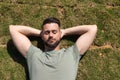 Young and handsome man, with a beard and green shirt, with his eyes closed and his hands behind the back of his neck lying on the Royalty Free Stock Photo