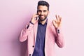 Young handsome man with beard having conversation talking on the smartphone doing ok sign with fingers, smiling friendly gesturing Royalty Free Stock Photo