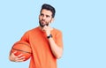 Young handsome man with beard hoilding basketball ball serious face thinking about question with hand on chin, thoughtful about