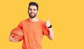 Young handsome man with beard hoilding basketball ball smiling happy and positive, thumb up doing excellent and approval sign Royalty Free Stock Photo