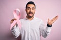 Young handsome man with beard holding pink cancer ribbon over isolated background very happy and excited, winner expression Royalty Free Stock Photo