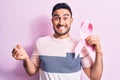 Young handsome man with beard holding pink cancer ribbon symbol over isolated background screaming proud, celebrating victory and Royalty Free Stock Photo