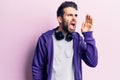 Young handsome man with beard listening to music using headphones shouting and screaming loud to side with hand on mouth Royalty Free Stock Photo