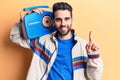 Young handsome man with beard listening to music using vintage boombox smiling with an idea or question pointing finger with happy