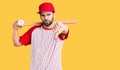 Young handsome man with beard playing baseball holding bat and ball with angry face, negative sign showing dislike with thumbs Royalty Free Stock Photo