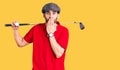 Young handsome man with beard playing golf holding club and ball covering mouth with hand, shocked and afraid for mistake Royalty Free Stock Photo